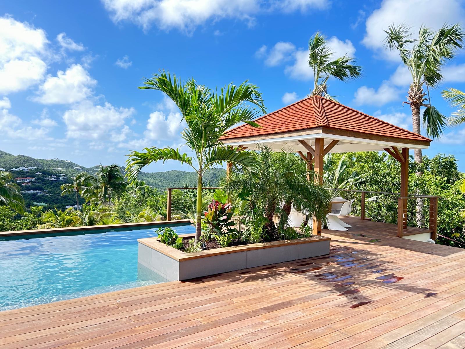 Poolside gazebo with tropical plants and wooden deck at a luxury St Barts villa overlooking the hills