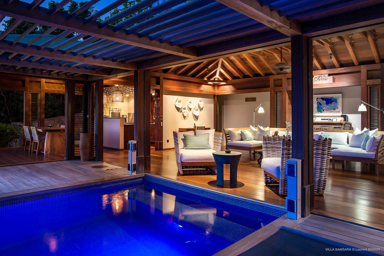 Evening view of a St Barts villa with illuminated pool and open-air lounge under wooden pergola