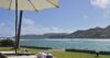Sun loungers under a white umbrella overlooking turquoise waters and coastal hills at a St Barts beachfront villa.