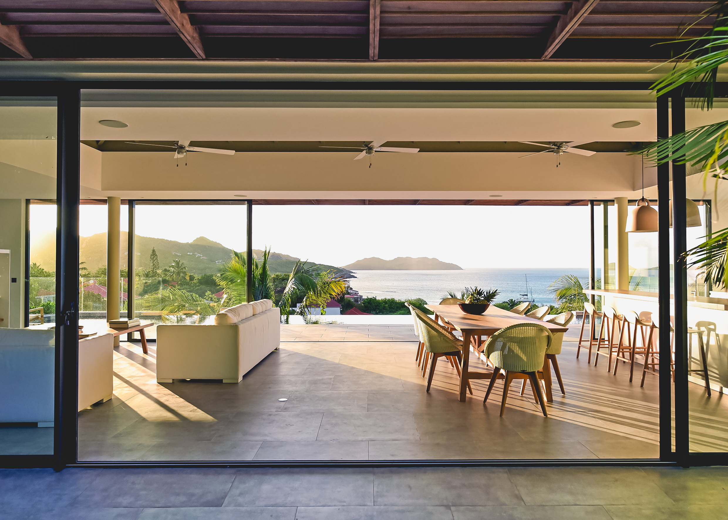 Open-air living and dining space in a St Barts villa with ocean views at sunset and modern island décor..