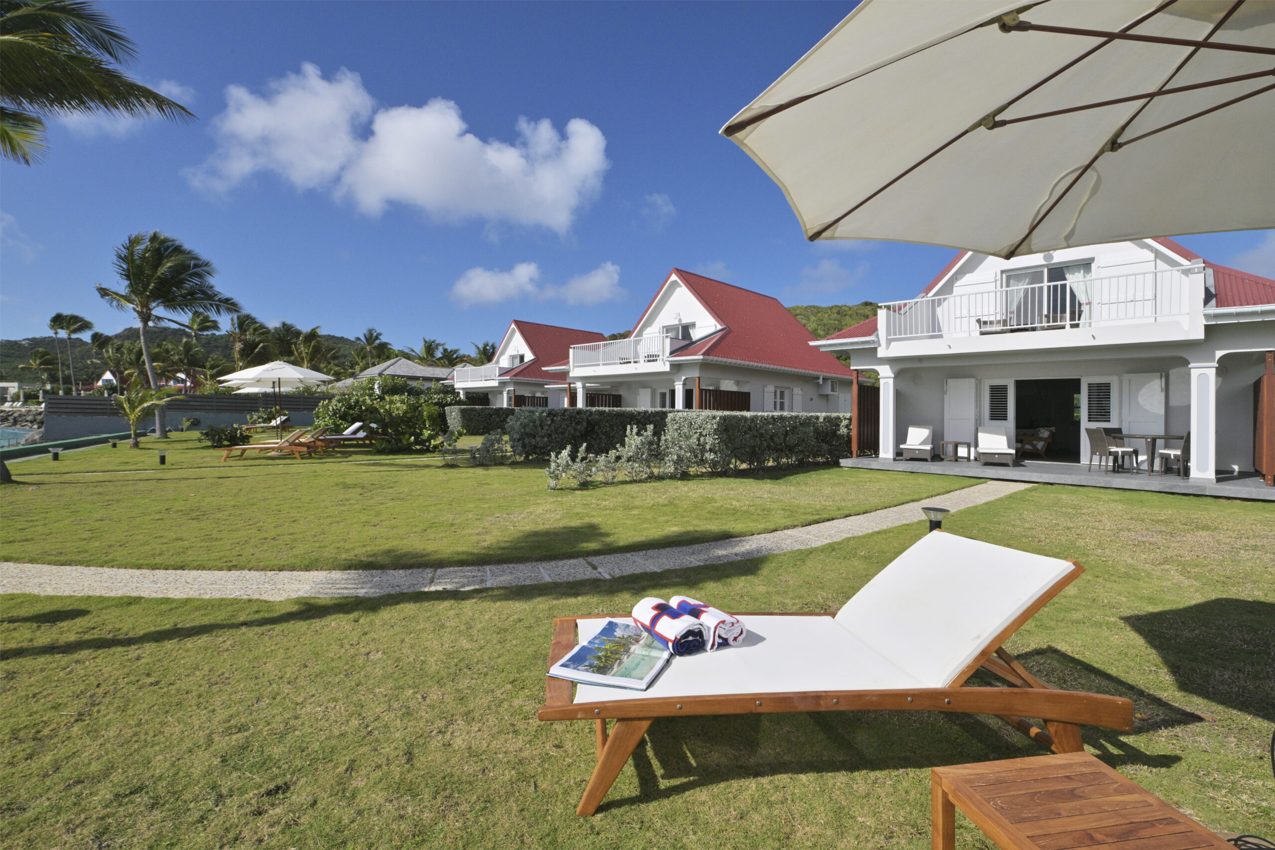 Beachfront villas with red roofs, private balconies, and sun loungers on a green lawn in St Barts vacation rentals.