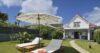 Garden with sun loungers and large umbrella facing a white villa with red roof in St Barts vacation rental.