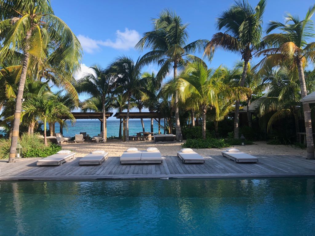 Poolside deck with sunbeds surrounded by palm trees overlooking the beach at a St Barts villa rental