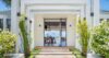 Elegant entrance of a St Barts villa framed by greenery, leading to open interiors with ocean views beyond.