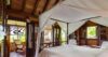 Tropical bedroom in St Barts villa with canopy bed, wooden interiors, and garden view.