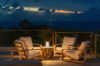 an outdoor seating area with four light-colored wood chairs and a small table on a deck at dusk, with the ocean in the distance.