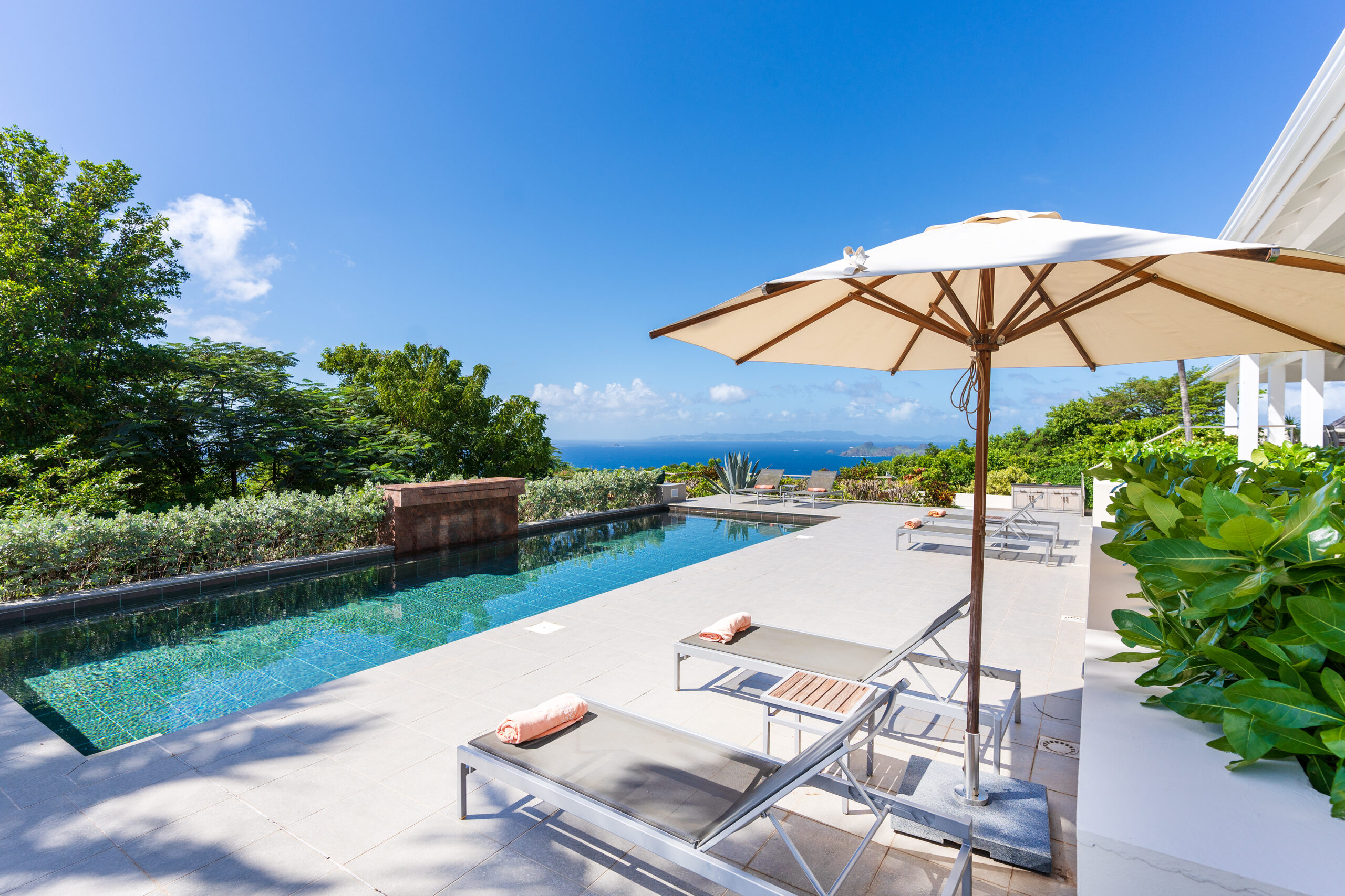 a side view of the infinity pool and pool deck, with two sunbeds and a large umbrella for shade, overlooking the ocean.