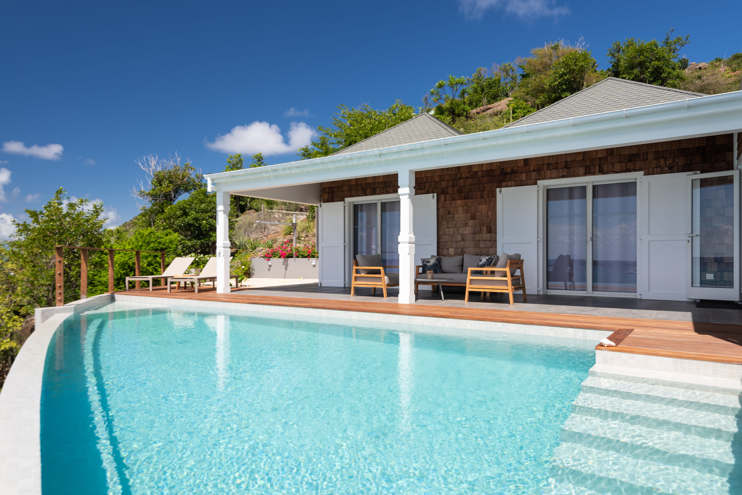 St Barts villa with turquoise infinity pool, sun loungers, and covered terrace framed by tropical hillside