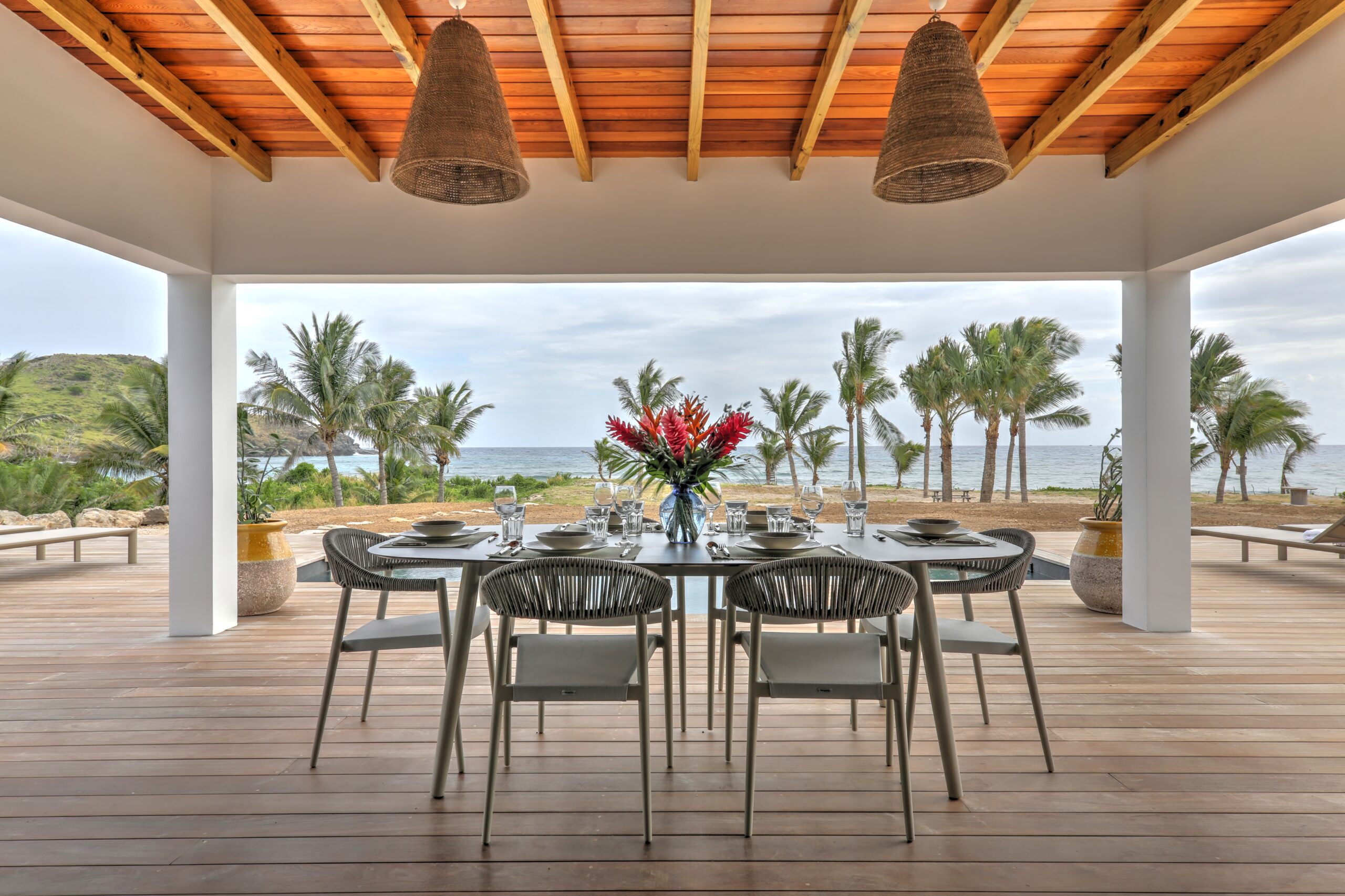 Covered dining terrace with tropical flower centerpiece and ocean views at a St Barts villa rental.