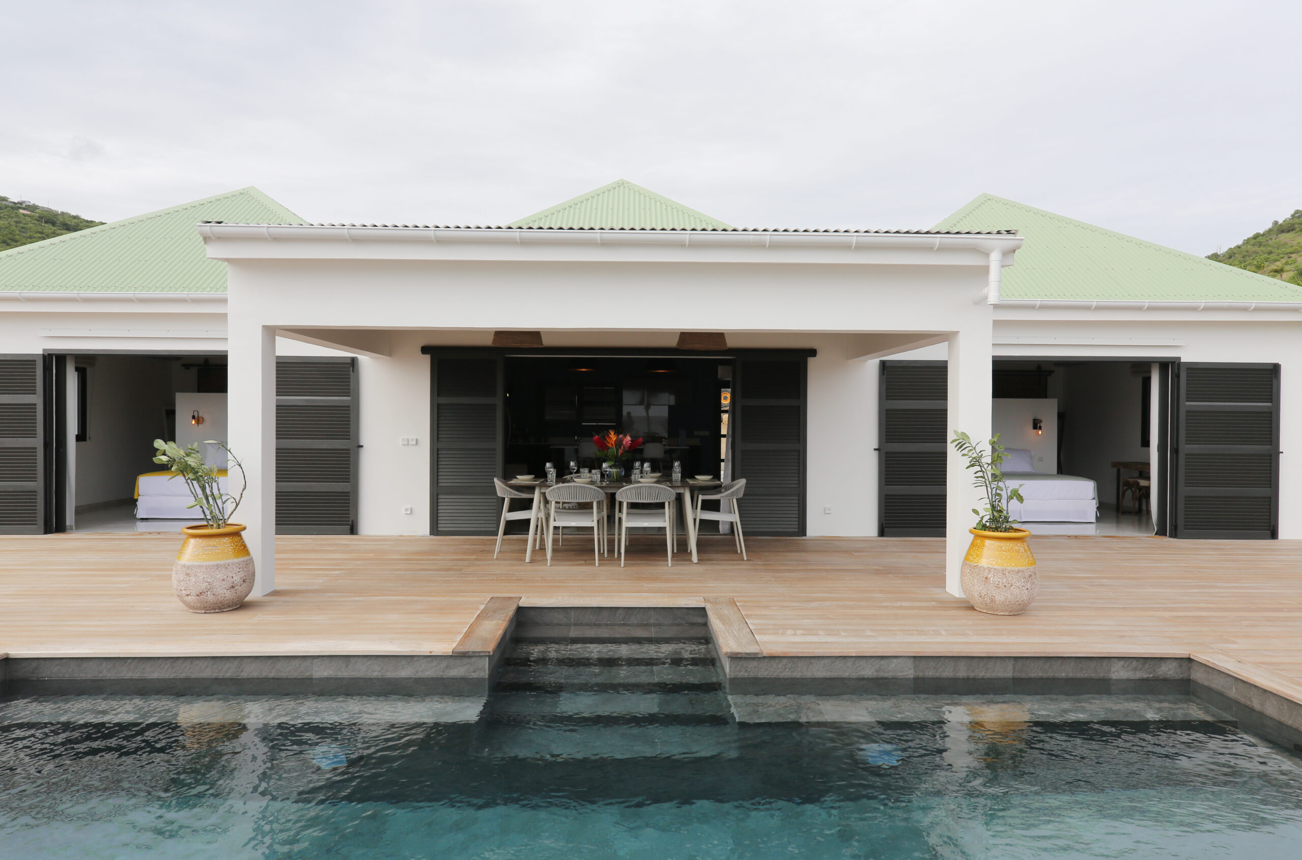 Poolside dining terrace with modern villa façade and green rooftops in St Barts.