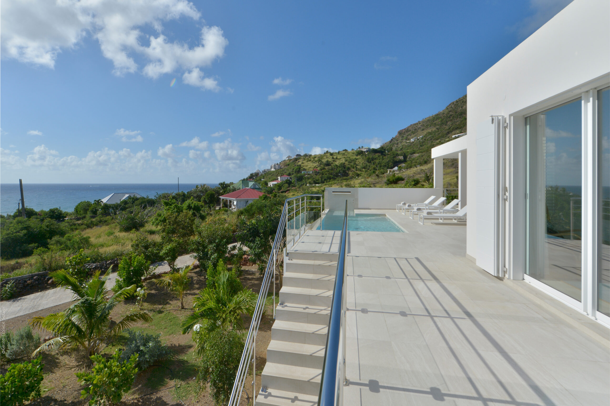 Spacious villa terrace with pool and ocean views surrounded by lush hills in St Barts.
