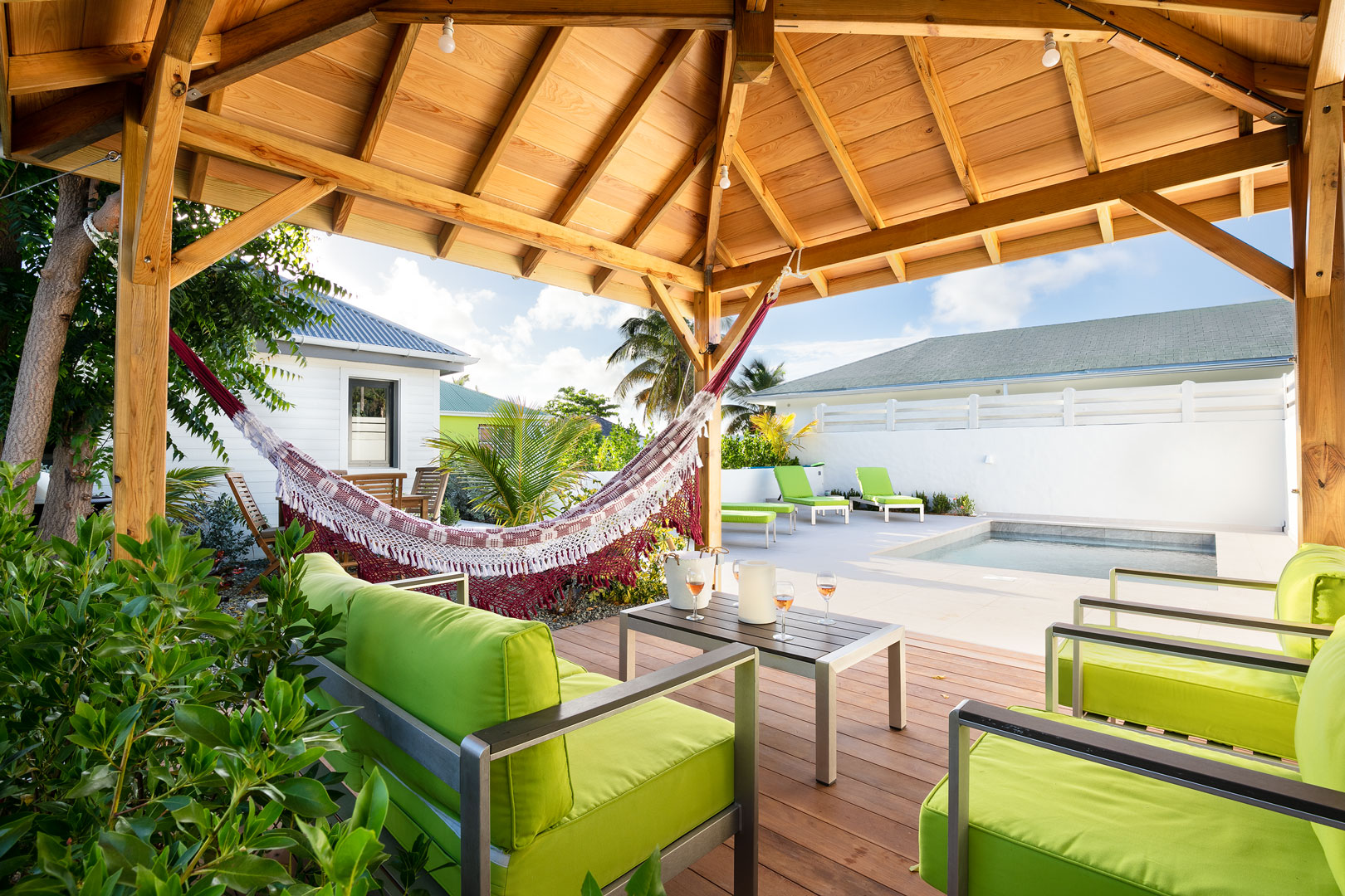 Shaded gazebo at a St Barts villa with hammock, green cushioned seating, and view of the private pool.