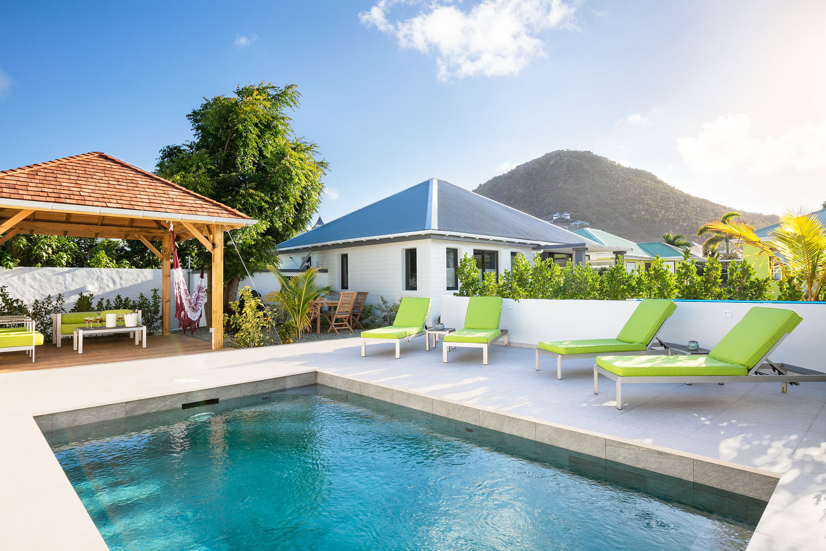 Private villa pool in St Barts with green sun loungers, shaded gazebo, and mountain views in the background