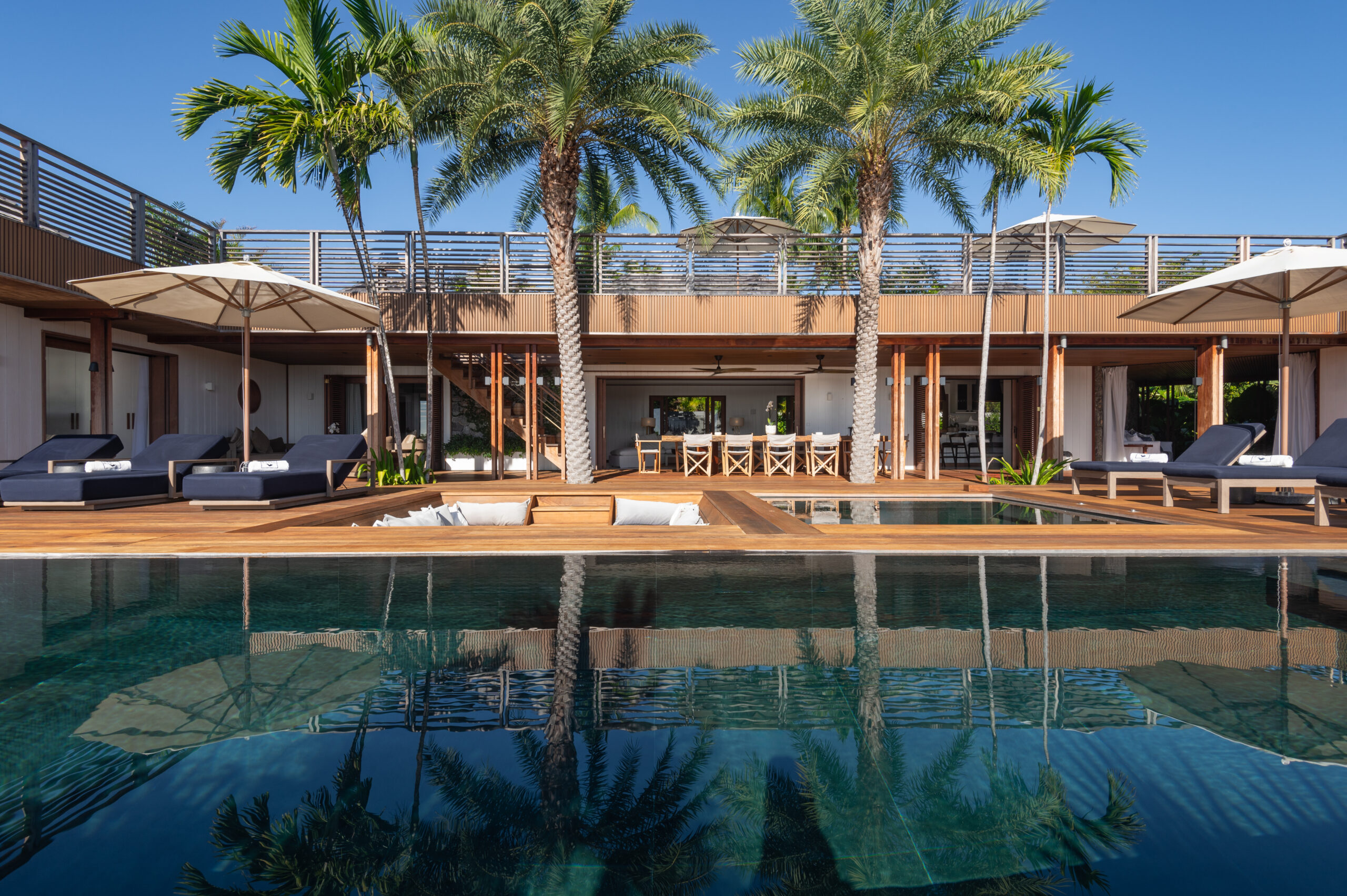Luxury St Barts villa with palm trees, shaded loungers, and a wooden deck surrounding a sparkling pool and outdoor dining area.