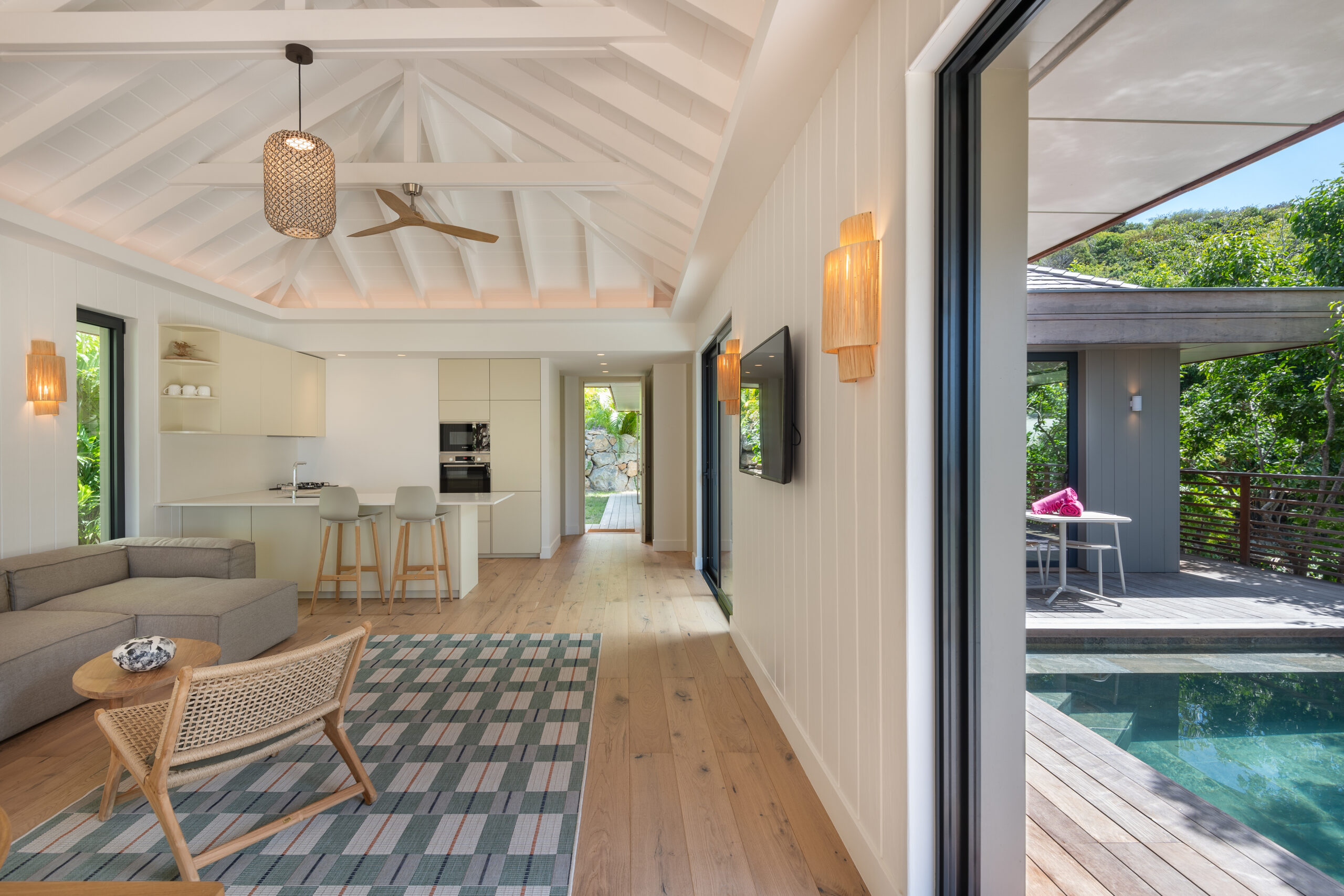 Stylish open-plan living room in a St Barts villa with vaulted ceiling, modern kitchen, and glass doors to the pool deck.