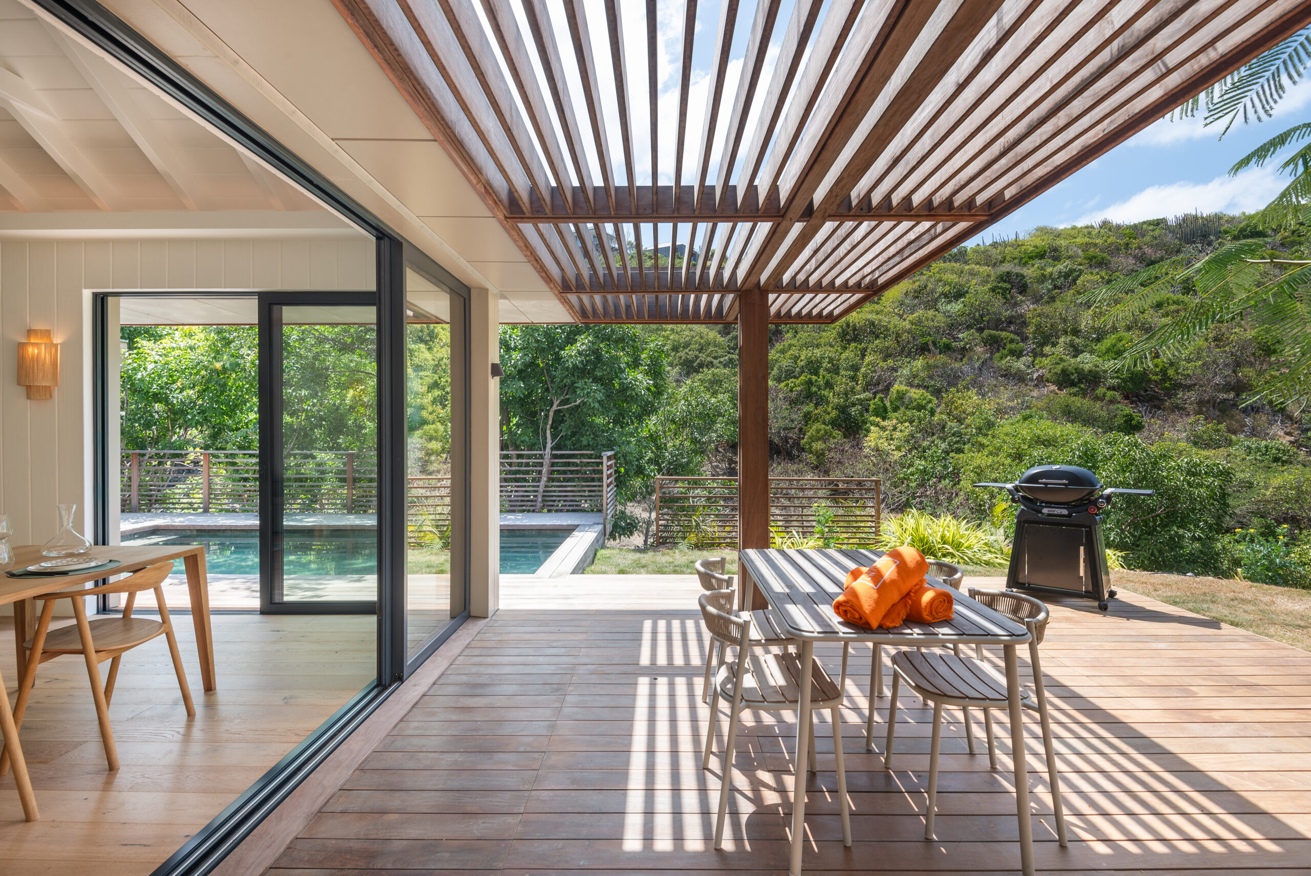 Shaded terrace of a St Barts villa with wooden pergola, outdoor dining table, and views of lush hillsides and pool.