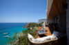 Terrace lounge at a St Barts villa with cushioned seating, wooden deck, and panoramic views over turquoise waters and anchored yachts.