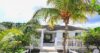 Charming St Barts villa with white picket fence, tropical garden, and shaded terrace framed by palm trees.