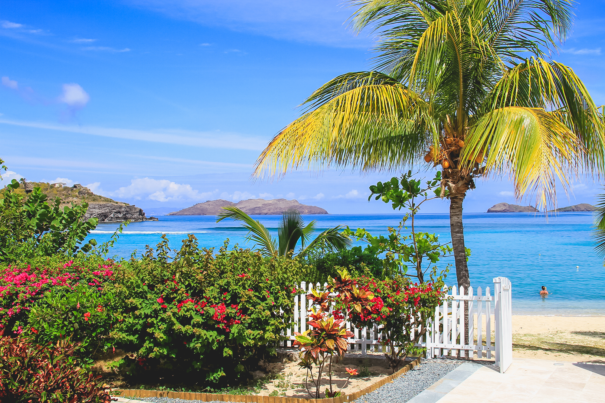 Beachfront St Barts villa with tropical garden, white picket fence, and turquoise Caribbean Sea views with offshore islands.