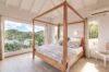 Sunlit villa bedroom with wooden four-poster bed and panoramic hillside views in a St Barts luxury rental.