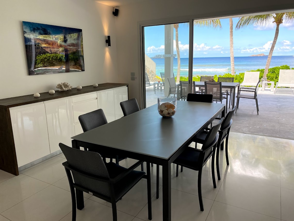 Dining area in a St Barts villa with sleek black table, glass doors to terrace, and panoramic ocean views.
