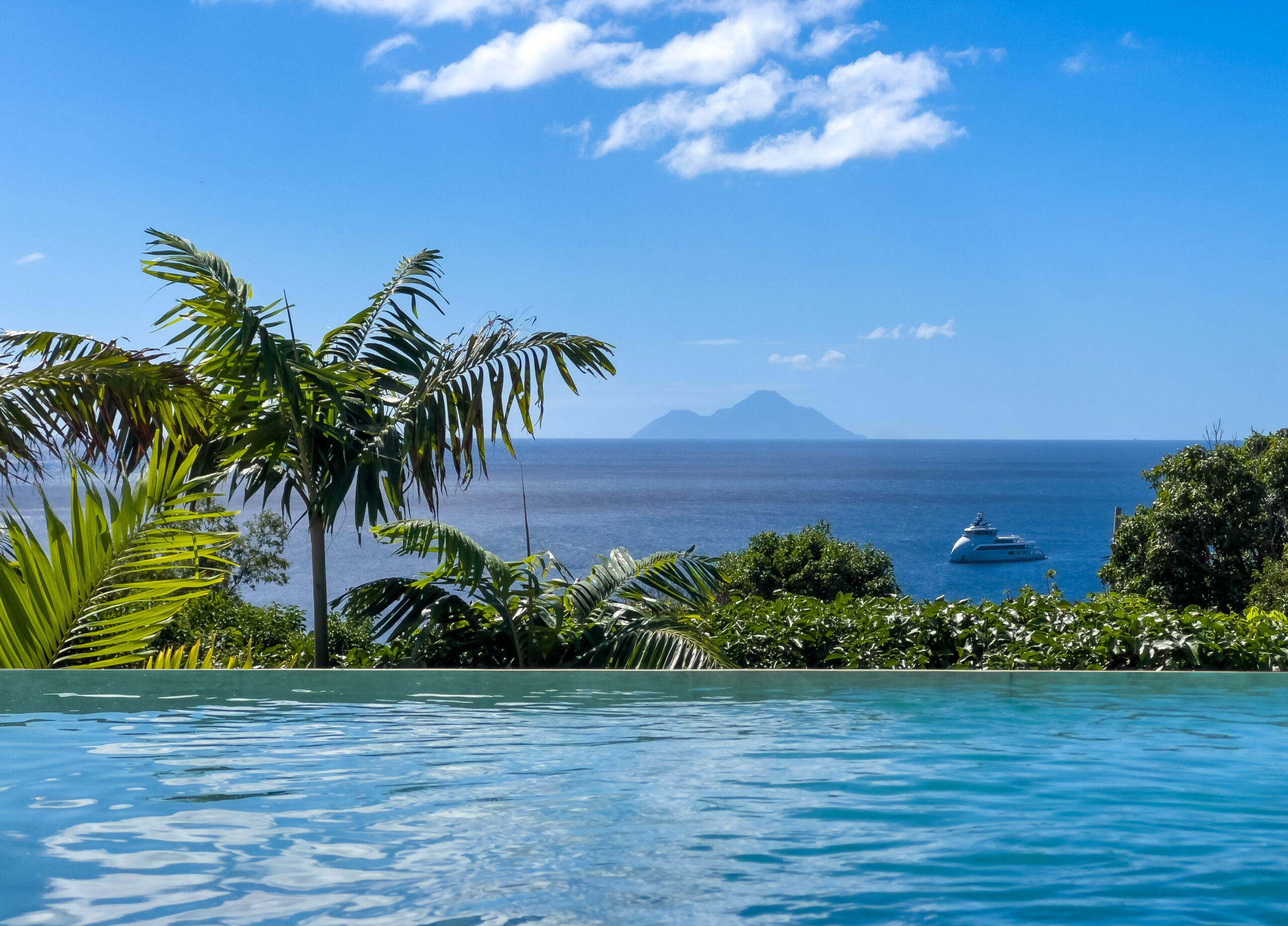 Infinity pool at luxury villa St Barths with ocean views, tropical palms, and distant yacht on the horizon