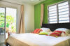 Colorful bedroom in a St Barts villa with green accent wall, striped pillows, and doors opening to tropical garden views.