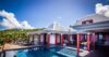 Colorful St Barts villa with red accents, shaded terrace, and pool deck surrounded by lush tropical hills.