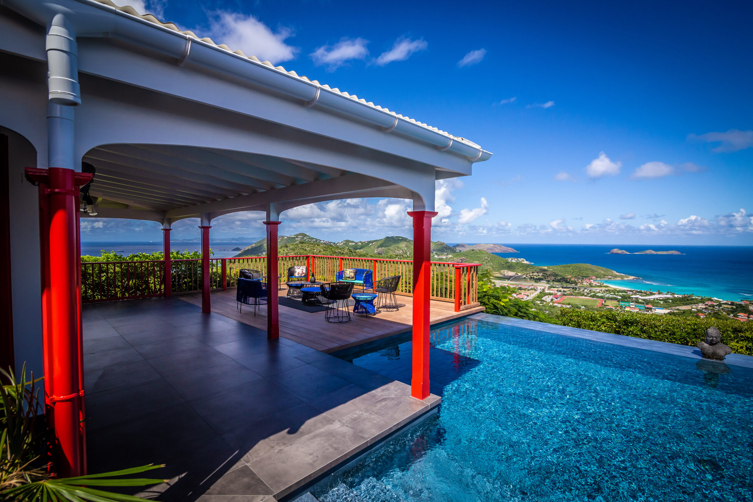 St Barts villa with infinity pool, red-accented columns, and sweeping views of turquoise sea and green hills.