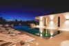 Night view of an illuminated infinity pool at a St Barts villa with sleek loungers and modern architecture under a deep blue sky.