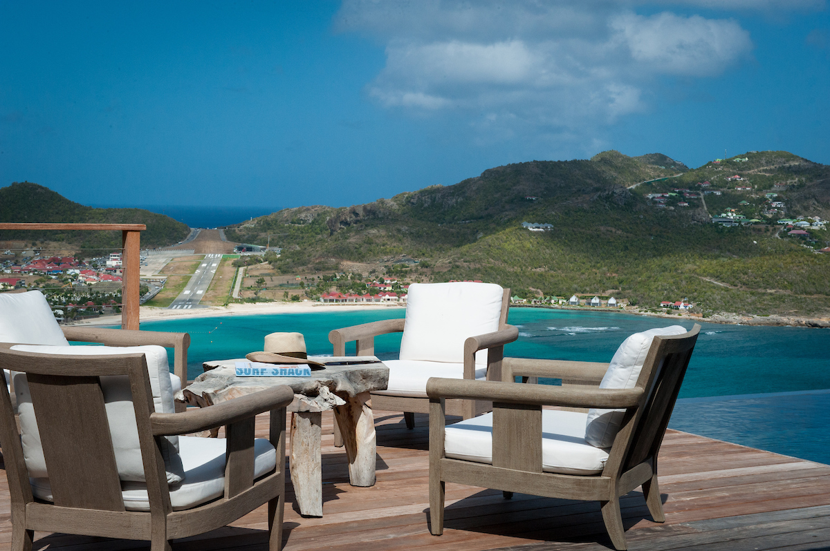 Terrace seating area at a St Barts villa with cushioned chairs overlooking turquoise waters and hillside runway views.