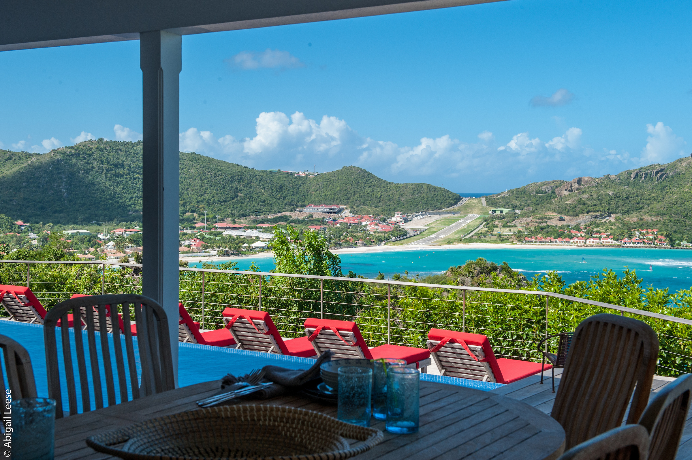 Covered terrace dining table overlooking pool loungers and turquoise bay views at a hillside St Barts villa rental.