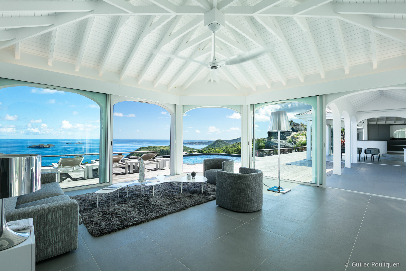 A luxurious modern living room with large windows that open to a deck with a pool and an ocean view.