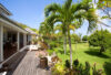 Garden terrace of a St Barts villa with tropical palms, flowering plants, and a wooden deck overlooking a lush green lawn.