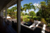 Shaded veranda at a St Barts villa with cushioned lounge seating overlooking a tropical garden with palm trees.
