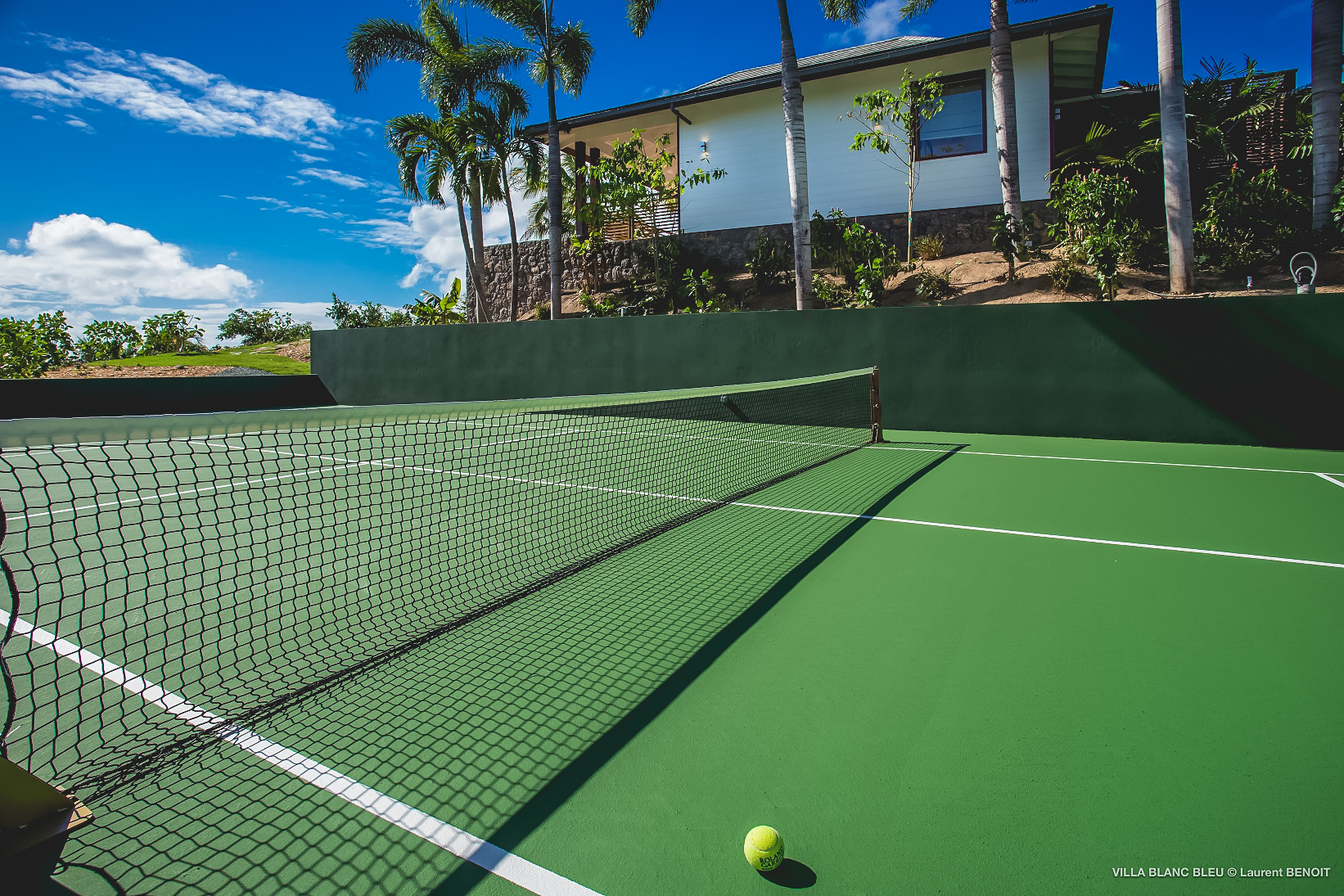 Private tennis court at a St Barts villa surrounded by palm trees and tropical landscaping