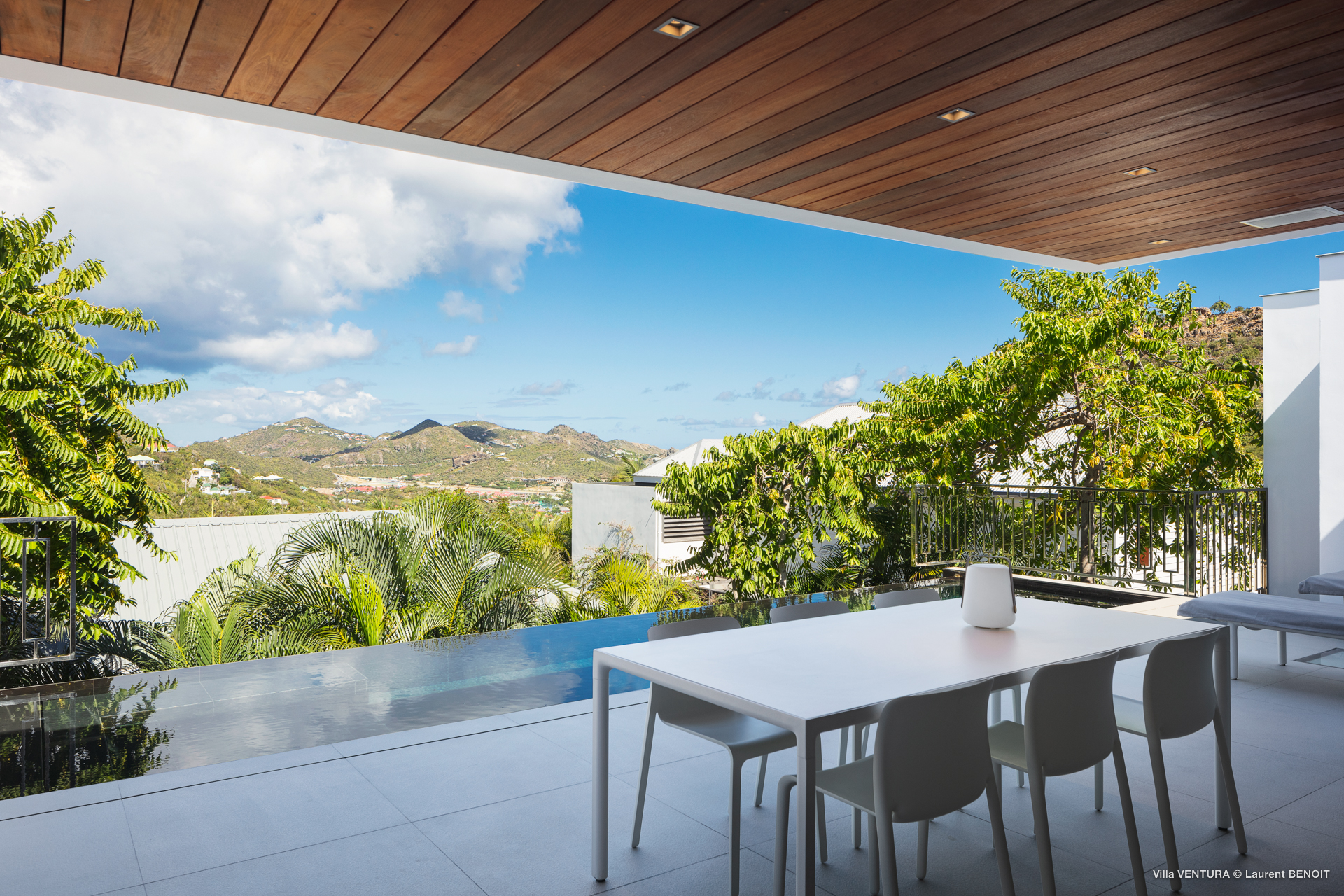 Covered terrace dining area in St Barts villa overlooking infinity pool and island hills.