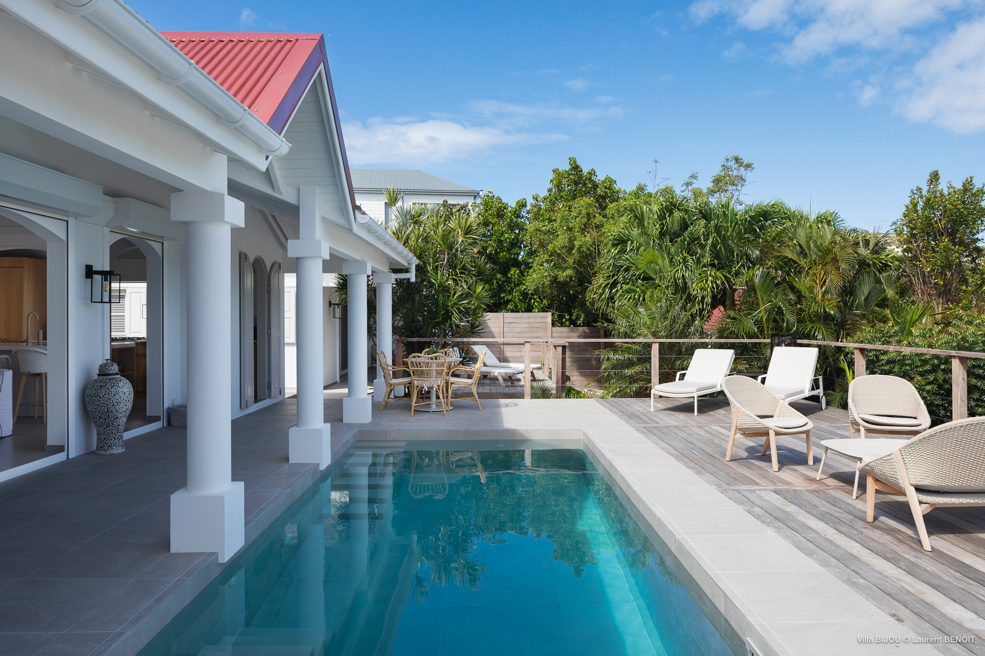 Private villa rentals in St Barts with a sleek poolside terrace, shaded dining area, and sun loungers framed by tropical greenery