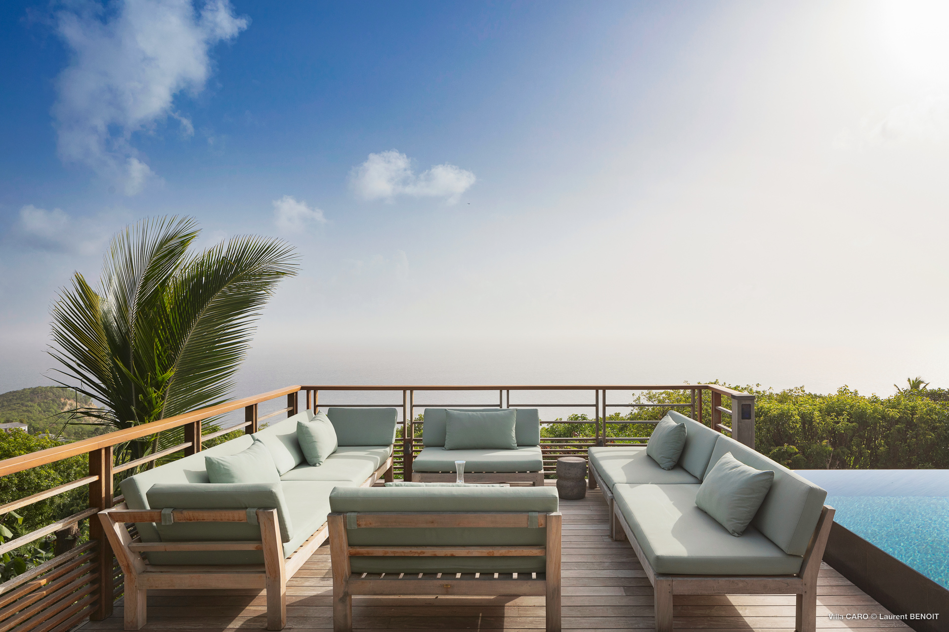 Outdoor lounge at a St Barts villa with cushioned sofas, wooden deck, and sweeping ocean views under a clear sky.