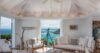 Elegant villa living room with white sofas, coastal décor, and panoramic ocean view framed by wide glass doors in St Barts.