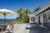 Sunny wooden deck with plunge pool, loungers, and ocean views surrounded by palm trees in a St Barts villa rental.