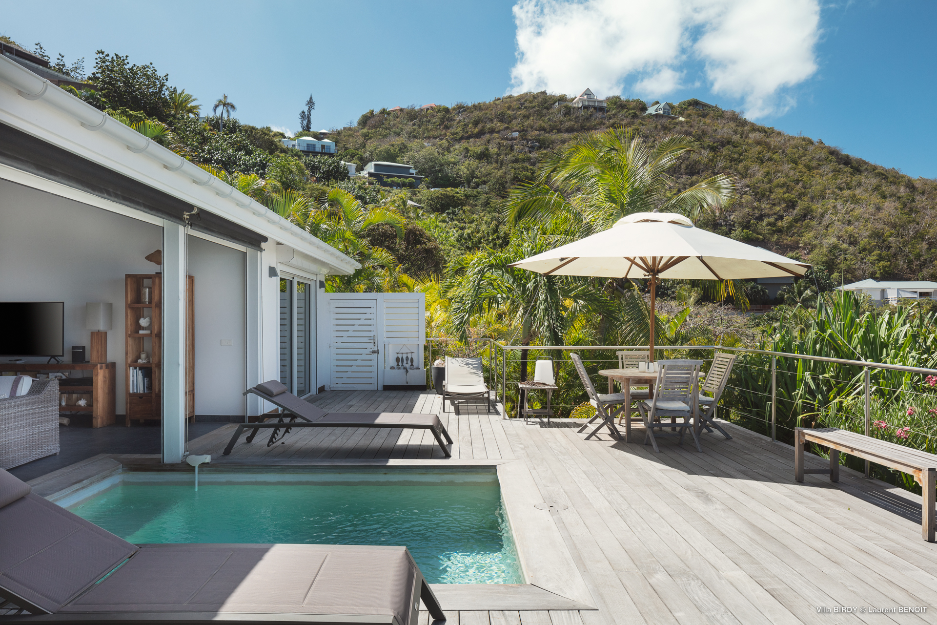 Private villa terrace in St Barts with pool, sun loungers, and shaded dining area overlooking tropical hills.