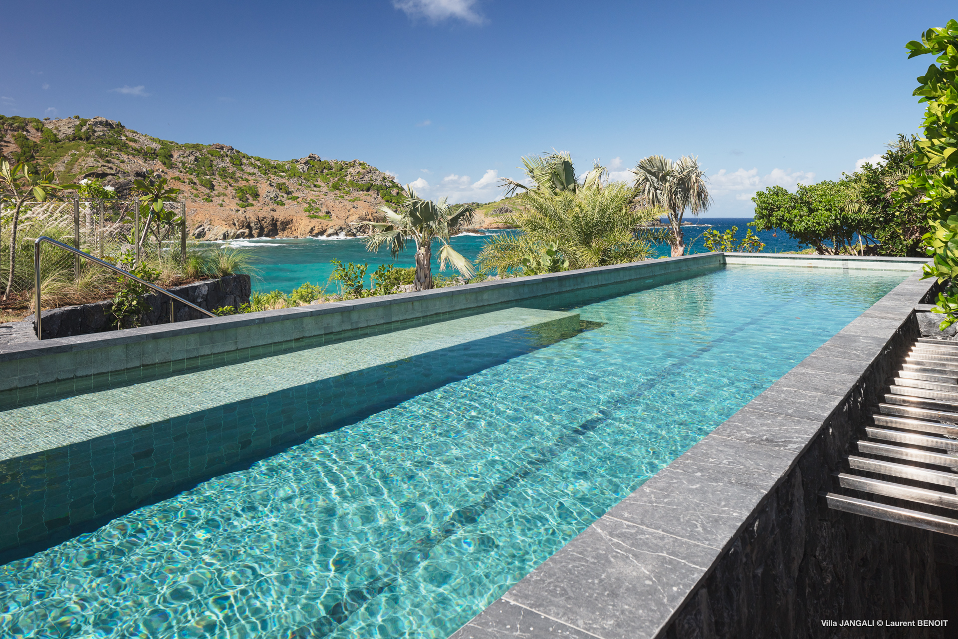 Long infinity pool with sun loungers, tropical garden, and ocean views at St Barts luxury villa