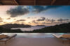 Sunset view from a St Barts villa infinity pool with lounge chairs overlooking the ocean and hills.