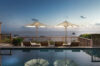 an infinity pool with its reflection of two large umbrellas and sun loungers, with a breathtaking sunset view over the ocean