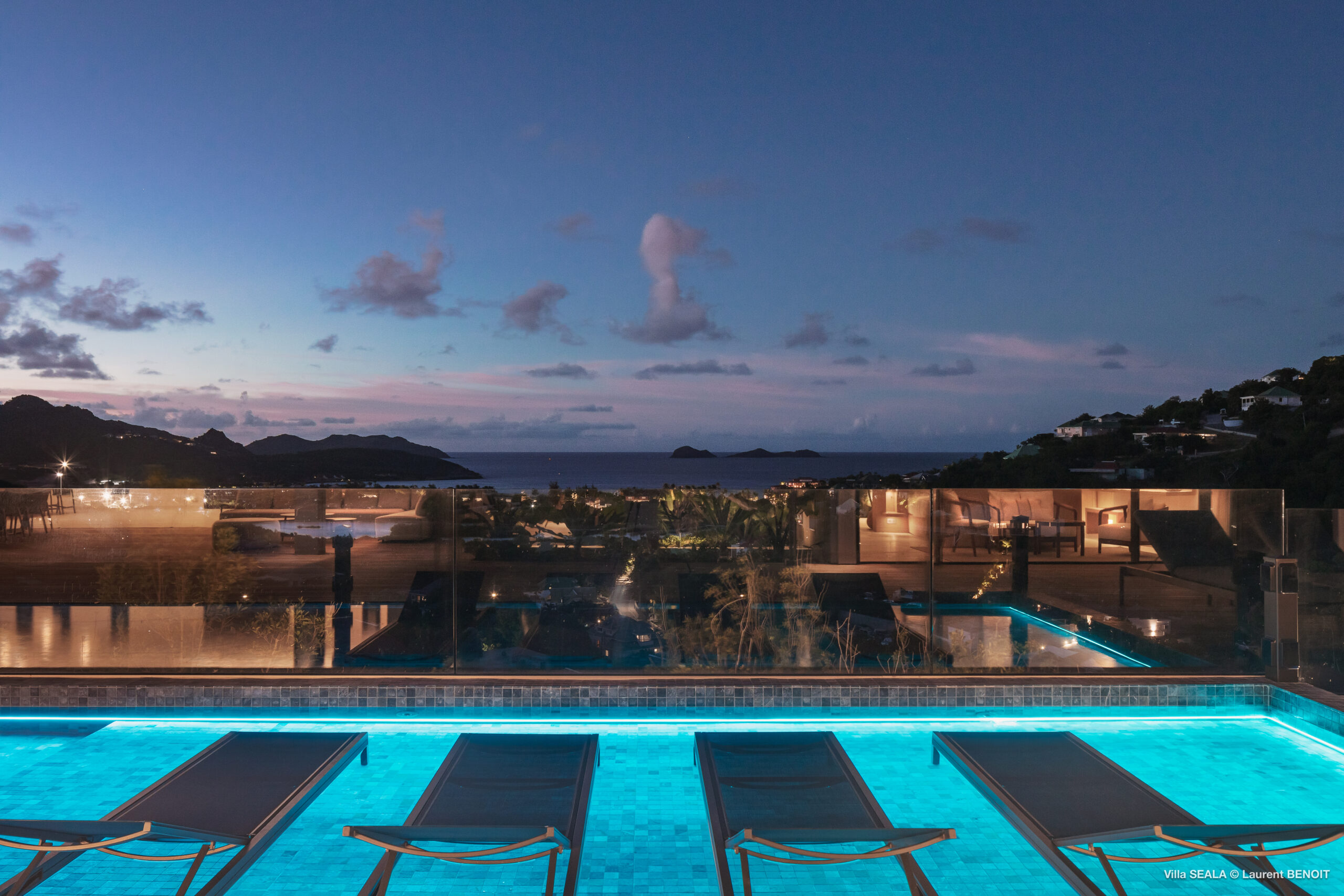 Evening view of illuminated infinity pool with loungers and ocean backdrop at a luxury St Barts villa