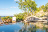 Secluded pool at a St Barts villa surrounded by rocks, tropical greenery, and wooden deck chairs with ocean glimpses beyond.