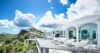 Expansive terrace of a St Barts villa with infinity pool, sun loungers, and sweeping views over lush hills and the sea.