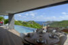 Terrace dining area in St Barts villa with infinity pool, sun loungers, and panoramic hillside ocean view.