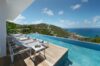 Infinity pool at a St Barts villa with sun loungers on a wooden deck overlooking green hills and the Caribbean Sea.